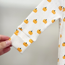 Load image into Gallery viewer, A close-up of a white long-sleeve baby sleeper that shows the convertible sleeves that can cover babys hands. The infant sleeper has an orange pumpkin print.
