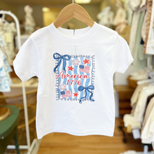 Load image into Gallery viewer, White toddler girls t-shirt with patriotic design that includes bows and flags with 'America 1776' design on a hanger inside Gracie Lou children's boutique