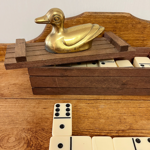 The vintage box with brass duck on top and showing some of the dominos that are contained in the box