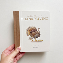 Load image into Gallery viewer, A hand holds a children's hardcover book titled "Our Little Adventure at Thanksgiving" against a plain light wall. The book has a cream cover with a brown spine, gold lettering, and an illustration of a turkey with a basket.