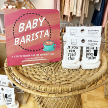 Load image into Gallery viewer, The book, Baby Barista, on a ratan table with socks that say "If you can read this, bring my mom a coffee".