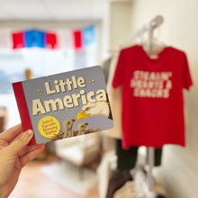 Load image into Gallery viewer, Person holding a book titled 'Little America' with a red t-shirt in the background.