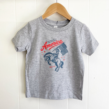Load image into Gallery viewer, Gray toddler t-shirt with 'America' graphic on a wooden hanger against a white background