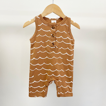 Load image into Gallery viewer, A brown sleeveless baby boy jumpsuit with a white wave pattern and a three-button henley neckline, hanging on a wooden hanger against a plain light background.