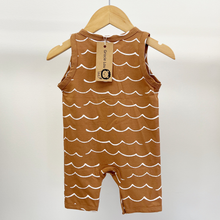 Load image into Gallery viewer, The back of a brown sleeveless baby boy jumpsuit with a white wave pattern and a three-button henley neckline, hanging on a wooden hanger against a plain light background.