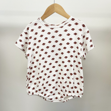 Load image into Gallery viewer, A white short-sleeve baby boy bubble romper hanging on a wooden hanger against a light gray wall. The garment is covered in a repeating pattern of small brown footballs,on cotton pointelle fabric, with snap buttons along the bottom.