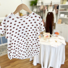 Load image into Gallery viewer, A white short-sleeve baby bubble romper with an all-over brown football print, on cotton pointelle fabric, hanging on a wooden hanger in Gracie Lou children's boutique setting.