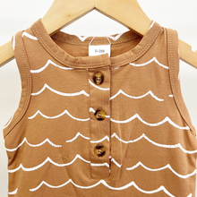 Load image into Gallery viewer, A sleeveless brown jumpsuit for infant boys, featuring a white wave line pattern and a three-button henley neckline, shown hanging on a wooden hanger.