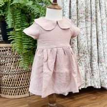 Load image into Gallery viewer, A dusty pink, linen children's dress on a baby size mannequin in front of a green fern on a wicker peacock chair and a floral adult women's dress. 