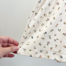 Load image into Gallery viewer, A close up of the skirt hem of an organic cotton baby dress that has an all over floral print in muted purples, blues, greens, and mustard colors.