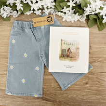 Load image into Gallery viewer, Light blue denim pants for kids with embroidered white daisy flowers, displayed on a wooden surface next to a children's book and a Gracie Lee tag.