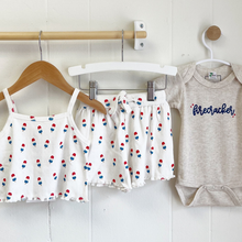 Load image into Gallery viewer, Summer baby clothing hanging on a white wall inside Gracie Lou children's boutique.
