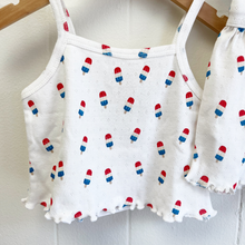 Load image into Gallery viewer, A close up picture of a white pointelle baby top and shorts set with bomb pop popsicle print on hangers against a white background.