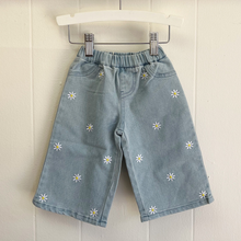 Load image into Gallery viewer, Light wash blue denim wide-leg jeans with white daisy flowers on a wooden hanger against a white background.