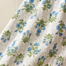 Load image into Gallery viewer, A close up detail to show the white dress with green and blue floral pattern fabric on a white background