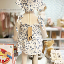 Load image into Gallery viewer, The back view of a baby mannequin wearing a floral romper and hat with a blurred children's store background