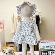Load image into Gallery viewer, Mannequin wearing a floral romper with a matching hat, surrounded by books and toys on a table.