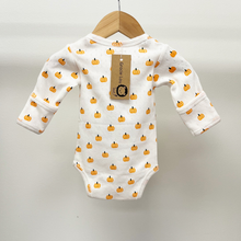 Load image into Gallery viewer, A white long-sleeve baby bodysuit with an all-over orange pumpkin print, on a white pointelle cotton fabric, hanging on a wooden hanger against a plain light gray background. A paper brand tag reading 'Gracie Lou' is attached to the back.