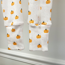 Load image into Gallery viewer, White cotton pointelle baby long sleeve sleeper with an all over pumpkin design is shown against a light gray wall inside the children's boutique, Gracie Lou. The long pants feature convertible footies and the close-up also shows the bottom of the two-way zipper.