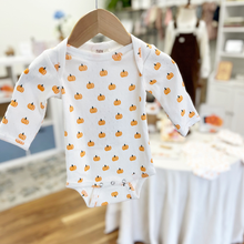 Load image into Gallery viewer, A white long-sleeve baby bodysuit with an all-over orange pumpkin print, hanging on a wooden hanger. The bodysuit features a snap button closure at the crotch.