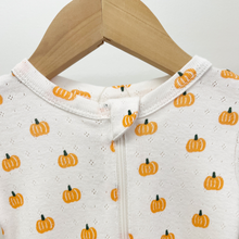 Load image into Gallery viewer, A close-up of a two-way-zip baby sleeper hanging on a wooden hanger against a plain light background. The item is white cotton pointelle fabric with an allover pumpkin print in orange. The top zipper is shown with fabric to cover the zipper.