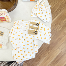 Load image into Gallery viewer, A baby clothing set laid flat on a light fabric surface, including a long-sleeve white top and matching bottoms printed with small yellow-orange pumpkins, plus an optional matching hat. Three kraft tags read 'Gracie Lou' with a lion logo.