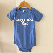 Load image into Gallery viewer, A heather blue baby bodysuit with 'BIRTHDAY boy' printed in white on the front, hanging from a wooden hanger against a light beige wall.