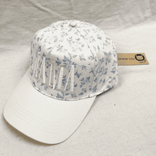 Load image into Gallery viewer, Floral-patterned cap on a light gray background, featuring a brand tag.