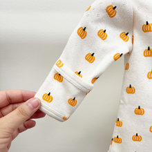 Load image into Gallery viewer, A close-up of a baby bodysuit convertible sleeve with a white pointelle cotton fabric and an orange pumpkin print, held by a hand to show the fabric texture and cuff detail.