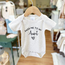 Load image into Gallery viewer, A baby short-sleeve bodysuit in a light oatmeal heather fabric, hanging on a wooden hanger. The bodysuit features the text 'PASS ME TO MY Aunt' and a small heart printed in black on the front.