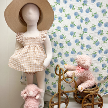 Load image into Gallery viewer, Mannequin wearing a checkered gingham top and bloomers with a straw hat, surrounded by pink piggy stuffed animals and a vintage wooden bicycle against a muslin floral swaddle blanket hanging on a wall.