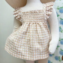 Load image into Gallery viewer, Baby mannequin wearing a checkered gingham top and bloomer set with a blurred floral background