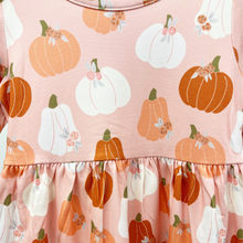 Load image into Gallery viewer, A close-up of a children's dress featuring an all-over autumn pumpkin print on a dusty pink background. The pattern includes orange and white pumpkins with small green stems and white flowers.