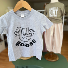 Load image into Gallery viewer, A Silly Goose tee shirt being held in front of a toddler mannequin that is wearing "A Little Dirt Never Hurt" tee shirt and striped linen pants.