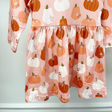Load image into Gallery viewer, A close-up of a children's dress with a pink base and an all-over pumpkin and white pumpkin print, hanging against a light gray wall.