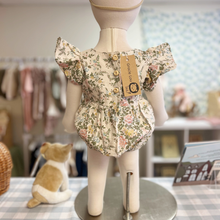 Load image into Gallery viewer, The back detail of a floral baby romper on a mannequin with a Gracie Lou tag, standing on a table with a checkered cloth.