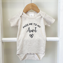Load image into Gallery viewer, A short-sleeve baby bodysuit in light heather gray, hanging on a wooden hanger against a white wooden wall. The bodysuit features the text 'PASS ME TO MY Aunt' and a small heart printed in black on the front.