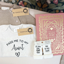 Load image into Gallery viewer, A styled flat-lay of baby gift items on a beige sofa: a light gray baby tee with the phrase 'PASS ME TO MY Aunt' and a heart, a taupe knit cardigan, a pink hardcover journal titled 'Aunt's Story,' and a pair of white socks with black text reading 'If you can read this to me my Aunt.' Two paper tags show the brand Gracie Lou.