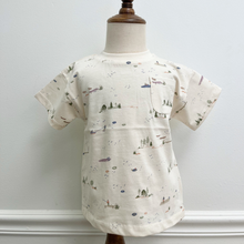 Load image into Gallery viewer, A short-sleeve toddler t-shirt in cream with a delicate, all-over watercolor-style print of boats, sailboats, ships, and small trees. The shirt features a classic crew neck and a left chest pocket, styled on a mannequin.