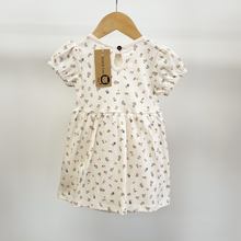 Load image into Gallery viewer, The back view of an organic cotton baby girl dress on a wooden hanger. The picture also shows a keyhole back with a single button at the neckline.