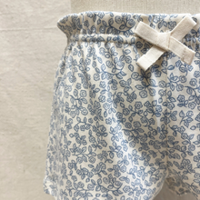 Load image into Gallery viewer, Close up detail of the tie on floral-patterned toddler shorts on a beige background