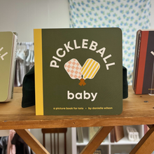 Load image into Gallery viewer, Children's book titled 'Pickleball Baby' on a wooden shelf with a blurred background