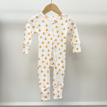 Load image into Gallery viewer, A baby long-sleeve footless one-piece sleeper hanging on a wooden hanger against a light gray wall. The sleeper is white with an all-over small orange pumpkin print.
