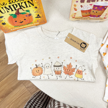 Load image into Gallery viewer, A light heather gray short-sleeve baby tee with a cute autumn-themed graphic of a pumpkin, ghost, acorn, leaf, and candy corn, styled on a light beige surface with a 'Gracie Lou' brand tag attached.