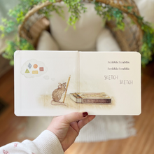 Load image into Gallery viewer, Hand holding a small book (titled: Scribble Scrabble) with illustrations of a mouse and a book, set against a blurred indoor background.
