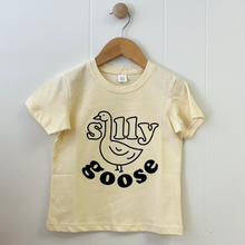 Load image into Gallery viewer, A butter yellow shirt with a Silly Goose print on the front of the shirt hanging on a white wall.