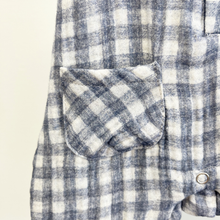 Load image into Gallery viewer, Close up details of the front pocket of a blue and white gingham, baby boy jumpsuit on a wooden hanger in front of a white background.