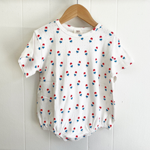 Load image into Gallery viewer, Baby bubble romper with red, blue, and white bomb pop popsicle pattern on a wooden hanger against a white wooden panel background.
