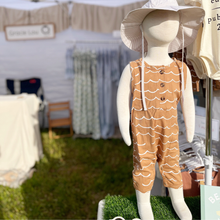 Load image into Gallery viewer, Baby boy mannequin wearing a brown sleeveless jumpsuit with white wave patterns, standing outdoors.