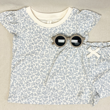 Load image into Gallery viewer, Floral-patterned toddler girls shirt and matching shorts with round sunglasses on a beige background.